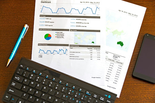 printed analytics reports alongside a black keyboard, blue pen, and smartphone